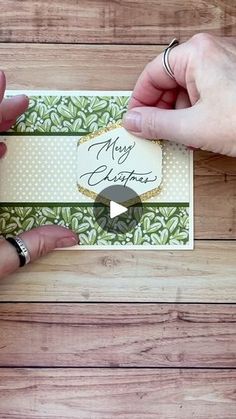 two hands holding a christmas card on top of a wooden table