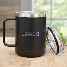 a black coffee mug sitting on top of a wooden table next to a glass jar