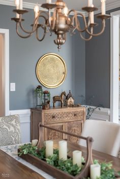 a dining room table with candles on it and a tray full of greenery in the center