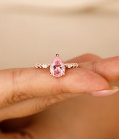 a woman's hand holding a pink ring with an oval shaped diamond in the middle