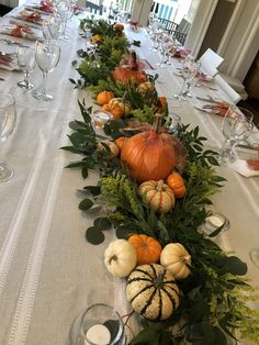 a long table is decorated with pumpkins and greenery