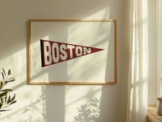 a framed boston pennant hangs on the wall next to a potted plant and window