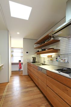 a kitchen with wooden cabinets and white tiled walls, along with a child standing in the doorway