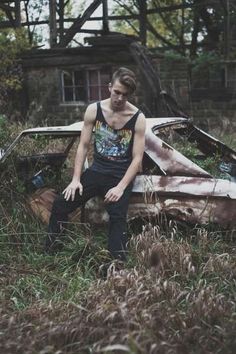 a young man sitting on the hood of an old car in front of a house