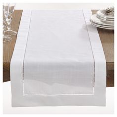 a white table runner on a wooden table with wine glasses and plates in the background