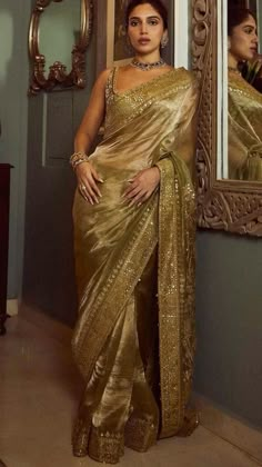 a woman in a gold sari standing next to a mirror