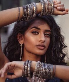 a woman with bracelets and rings on her head is posing for the camera while holding her hands behind her head