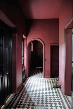 an empty hallway with black and white checkered flooring, red walls and doors