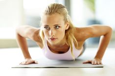 a woman is doing push ups on the floor with her hands behind her head and looking at the camera