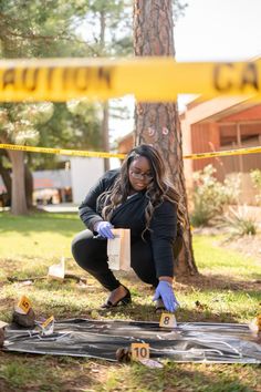 a woman in black jacket and blue gloves kneeling down next to tree with yellow caution tape on it