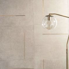 a floor lamp in front of a white wall with lines on it and a round glass ball hanging from the side