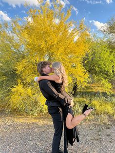 a man and woman kissing in front of a yellow tree