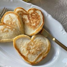 three heart shaped pancakes on a white plate with a fork and knife next to them