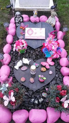 a table with pink rocks and flowers on it in the middle of a grave yard