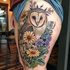 an owl and flowers tattoo on the back of a woman's thigh, which is covered in tattoos