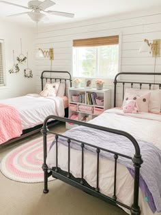 two twin beds in a bedroom with pink and white bedding, rugs on the floor