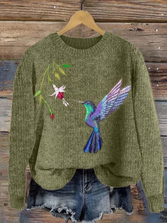 a green sweater with a hummingbird and flowers on it, hanging from a hanger