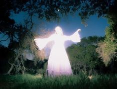 a person standing in the grass with their arms spread out and lights shining on them