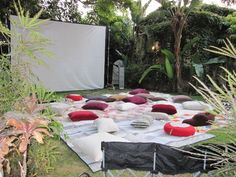 an outdoor movie is set up in the backyard with lots of pillows and blankets on it