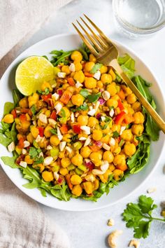 a white plate topped with salad next to a glass of water and a yellow fork