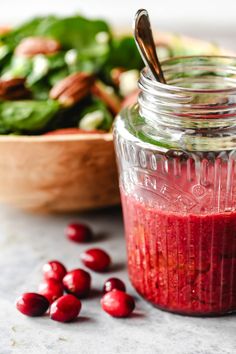 a glass jar filled with cranberry sauce next to a bowl of spinach