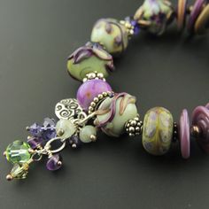 "Like a breath of Spring, you'll love the feel of this handmade lampwork and sterling silver bracelet. The handmade glass beads are combined here with Swarovski crystals and Sterling silver in this one-of-a-kind bracelet. A cluster of Swarovski crystals, and gemstone rondelles including aquamarine and amethyst accents the gorgeous beads in purple, burgundy, celadon, sage and more. A decorative sterling silver butterfly toggle clasp and a dangle of coordinating crystals and gemstones complete the Artisan Czech Glass Beaded Bracelets With Spacer Beads, Lampwork Glass Beads Jewelry, Collage Jewelry, Lampwork Bracelets, Green Board, Lampwork Bead Jewelry, Purple Burgundy, Fashion Beads, Glass Beads Jewelry