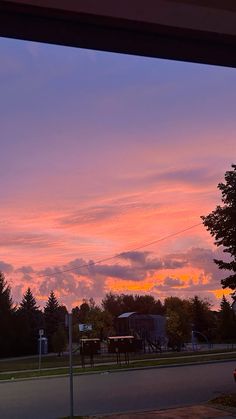 the sky is pink and purple as the sun sets in the distance behind some trees