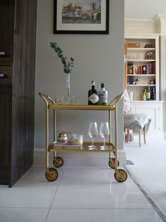 a bar cart with wine glasses and bottles on it in front of a framed photograph