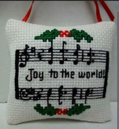 a cross stitch pillow with musical notes and holly wreaths on it that says joy to the world