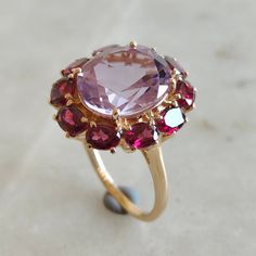 This stunning ring is set in 14k Solid Yellow Gold with Natural Pink Amethyst & Rhodolite Garnet with utmost precision. It is a unique statement gemstone ring for nearly every occasion and is completely hassle-free jewelry. ITEM DETAILS: * CENTER GEM: Pink Amethyst * GEM SIZE: 10X12mm * GEM SHAPE: Oval * SIDE GEM: Rhodolite Garnet * GEM SIZE: 4x3mm  * GEM SHAPE: Oval * Total Gem weight: 6.85 carats * Gold Purity: 14KT  * Gold Weight: 3.15 gram * Total Weight of the Ring: 4.52gram The Gold purity Fine Jewelry 14k Gold Amethyst Ring With Halo Setting, 14k Gold Multi-stone Amethyst Ring, Heirloom Multi-stone Amethyst Ring In 14k Gold, Amethyst And Garnet, Amethyst Wedding Rings, February Birthstone Ring, Rhodolite Garnet Ring, Amethyst Wedding, Gold Amethyst Ring