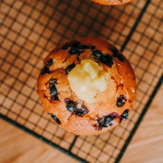 two blueberry muffins on a cooling rack with butter and raisins