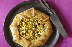 a small pizza on a black plate with a knife and fork next to the pie