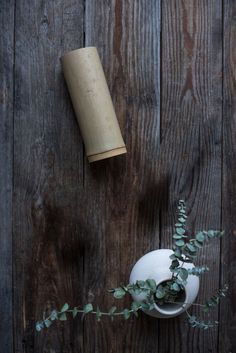 a white vase sitting on top of a wooden table next to a planter and a roll of toilet paper