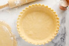 an uncooked pie crust sits on a marble countertop next to rolling dough