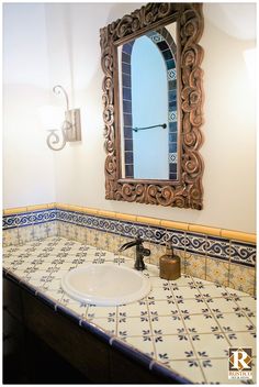 a bathroom sink with a mirror above it and tile on the counter top, along with a soap dispenser