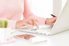 a woman is typing on her laptop while holding a pen and paper in her hand