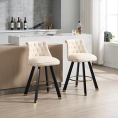 two white bar stools with black legs in front of a counter and wine bottles