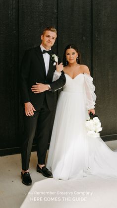 a bride and groom posing for a photo in front of a black wall with white flowers