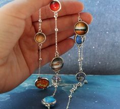 a hand holding some kind of necklace with planets on it's chains and beads