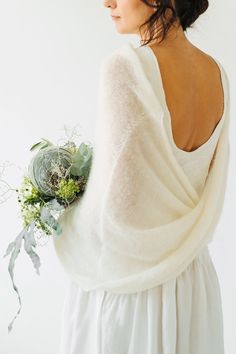 a woman wearing a white dress and holding a flower in her right hand, looking off into the distance