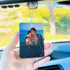 a person holding up a photo ornament in their car