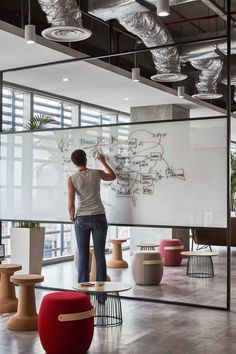 a man writing on a whiteboard in an office with lots of tables and stools