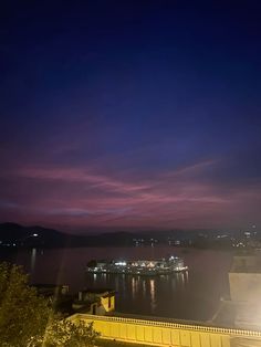 the night sky is lit up with colorful clouds over water and buildings in the distance