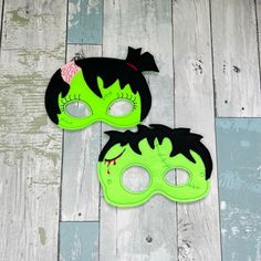 two children's masks with green and black paint on them, one has a pink flower in its hair