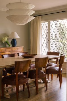 a dining room table with chairs and a vase on top of it in front of a window