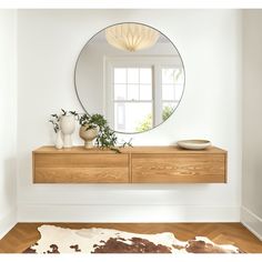 a mirror and vases on a wooden shelf in front of a window with a cow hide rug