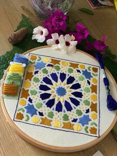 a cross stitch pattern on a wooden table with flowers and thread spools next to it