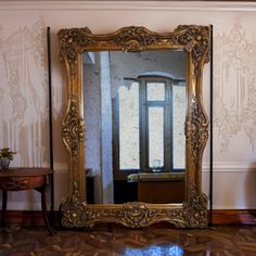 a large mirror sitting on top of a hard wood floor next to a table and chair