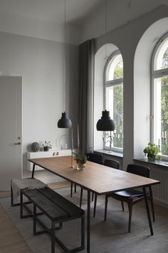 a dining room table and benches in front of two large windows with arched arches on the wall