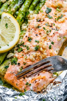 salmon and asparagus on foil with lemon wedges, garlic and parsley